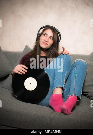 Attraktive junge Frau istening Musik mit Kopfhörer holding Schallplatte in den Armen Stockfoto