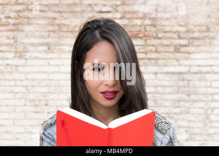 Junge latina Frau Porträt an Kamera suchen und lesen Rote Buch Stockfoto