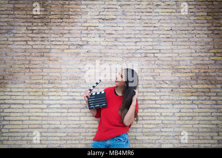 Junge hübsche Latina woman holding Filmklappe board mit Mauer im Hintergrund suchen Stockfoto