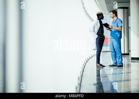 Zwei zuversichtlich, dass Ärzte, die sich in Halle etwas diskutieren und deutete auf die Zwischenablage auf modernes Krankenhaus Stockfoto