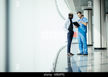 Zwei zuversichtlich, dass Ärzte, die sich in Halle etwas diskutieren und deutete auf die Zwischenablage auf modernes Krankenhaus Stockfoto