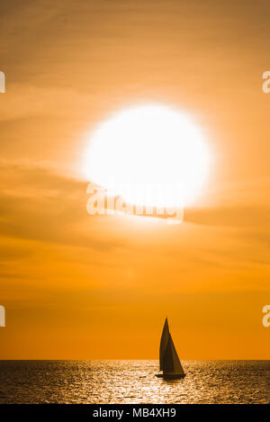 Segelboot Segeln auf dem Ozean während einer spektakulären Orange Tropical Sunset gegen den leuchtenden Himmel in einem Wider weg von Sonnenlicht Silhouette auf der Wat Stockfoto