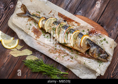 Ganze gebackene Makrelen oder scomber Fisch mit Zitrone und Grüns auf Papier, dunklen Hintergrund, Ansicht von oben Stockfoto