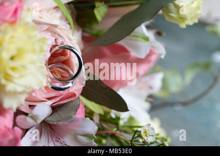 Nahaufnahme der beiden Hochzeit Ringe auf einem weißen und rosa Brautstrauß mit Betreff auf der linken Seite Stockfoto