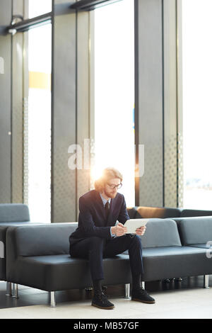 Junge elegante Geschäftsmann in Anzug sitzen auf einem Ledersofa von Airport Lounge und die Suche nach Informationen für neues Projekt im Netz Stockfoto