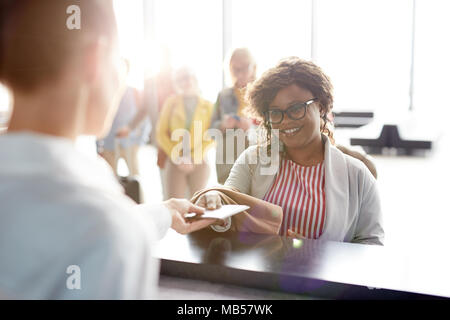 Glückliche junge Reisende geben Registrierung Manager ihr Reisepass für Check-in im Stehen durch Zähler Stockfoto