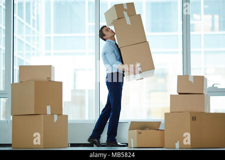 Junge Unternehmer, die riesigen Stapel von großen Boxen mit Büromaterial bei Umzug in ein modernes Business Center Stockfoto