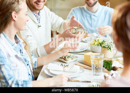 Junger Mann gießen hausgemachte Limonade im Glas von seiner Freundin beim Abendessen mit Freunden Stockfoto