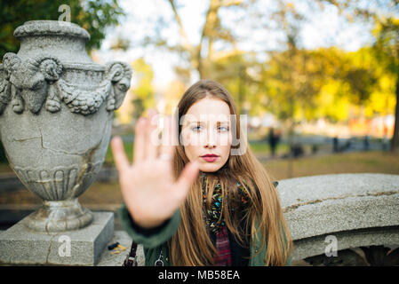 Attraktive junge Frau im Park ist unzufrieden und ein Stop-Schild mit ihren Händen Stockfoto