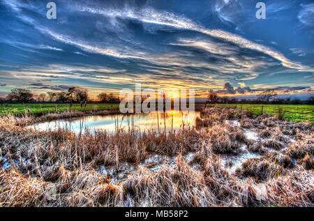 Dorf von Coddington, England. Künstlerische Sonnenuntergang Blick auf ein Süßwasser-Teich in einem Cheshire Landwirtschaft Feld. Stockfoto