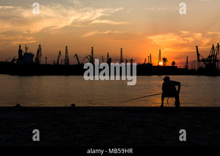 Silhouette eines Fischers gegen Silhouette der Kran in Varna Seehafen Stockfoto
