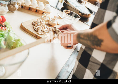 Ein Kerl mit einem Tattoo auf seinem Arm gehackten Gemüse auf einem Salat, Kochen in der Küche zu Hause. Innen-, Studio shot Stockfoto