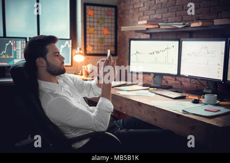 Junger bärtiger Mann Händler im Büro sitzen am Tisch Kontrolle smartphone nachdenklich entspannt Stockfoto