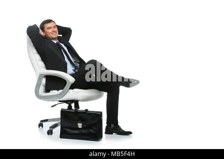 Hübscher junger Geschäftsmann in Business sut, blaues Hemd und Krawatte holding Aktenkoffer sitzt auf einem Sessel. glücklichen Ausdruck. Studio auf Weiß isoliert Schuß Stockfoto