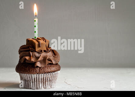 Eine Chocolate Caramel Cupcake mit auf dunkelgrauem Hintergrund Kerze angezündet - Platz für Text Stockfoto