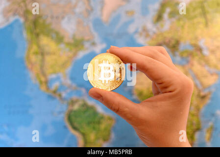 Hand, die Gold Medaille der Bitcoin gegen Karte der Welt. Bitcoin Konzept. Neue Welt Währung. Stockfoto