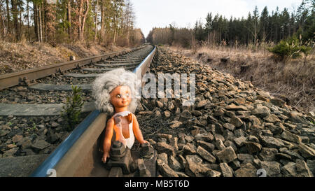 Kaputte Puppe auf der Schiene im sonnigen Wald landschaft. Verlorenes Kind Spielzeug am Alten rostigen railroad Track. Gefahr, Kindheit, Schicksal, Unfall, sci-fi, Krieg, Missbrauch. Stockfoto