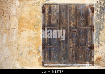 Geschlossen alte Holztür mit Metall rostig-Box öffnen und die Details zu einer Verwitterten gelbe Wand, Platz für Text. Mdina, Malta Stockfoto