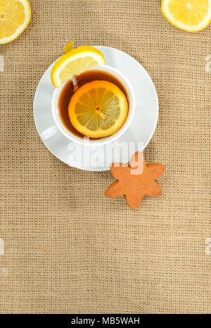 Eine Tasse Tee mit Zitrone und ein zwei halbe Zitronen in jeder Ecke und ein Stern Cookies auf sackleinen Hintergrund. Hochformat. Raum nach unten. Stockfoto