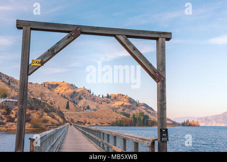 Holz Torbogen über ehemalige train trestle Brücke umgewandelt zu Wandern und Radfahren Trail mit Blick auf den See und die Berge in der Ferne bei Sonnenuntergang Stockfoto