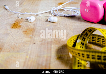 Stil leben mit rosa Gewichte, Ohrhörer und ein gelbes Band measrument. Fitness. Konzept Stockfoto