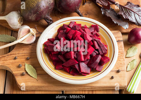 Rote Bete in Scheiben auf einen Teller mit frischen, roten Rüben, Knoblauch und Gewürzen im Hintergrund Stockfoto