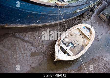 Zwei verwitterte Boote ruhen auf dickem Mündungsschlamm, während die Flut zurückgeht, und enthüllen Texturen, Schutt und die ruhige Stille einer funktionierenden Küste Stockfoto