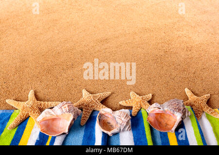 Beach border with towel, starfish and seashells.  Space for copy.  Sharp focus on the foreground objects.  Studio shot - directional lighting and warm Stockfoto