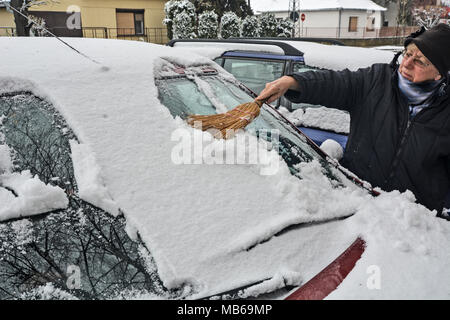 Treiber Reinigung Schnee aus der Halterung für die Windschutzscheibe eines Autos mit einer Bürste reinigen. Stockfoto