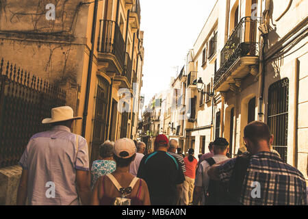 Touristen gehen hinunter eine Straße in Spanien. Einige Touristen tragen Kappen sind, ein älterer Mann trägt einen Hut. Stockfoto