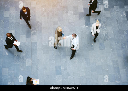 Von oben Geschäftsleute handshaking und Begrüßung in Halle voll der Organisation erfüllt. Stockfoto