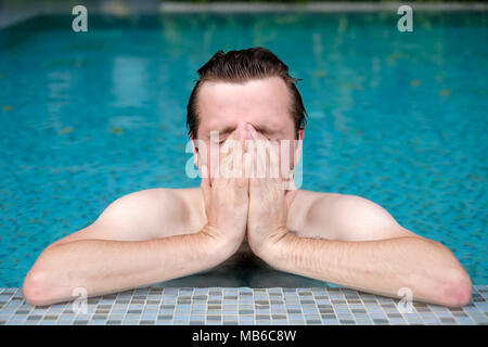 Ein junger Mann im Pool Tücher sein Gesicht mit der Hand. Er ist allergisch auf chlorierte Wasser. Stockfoto