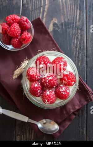 Raspberry cheesecake Dessert im Glas Glas mit frischen Himbeeren und Sahne Käse auf Holz- Hintergrund. Gesunde hausgemachte Sommer berry 2-in-1-Dessert. Stockfoto