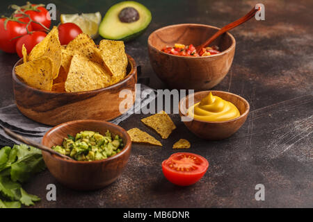 Mexikanisches Essen Konzept. Nachos - Mais, totopos Chips mit verschiedenen Saucen in mit Holz Schalen: Guacamole, Käse Sauce, Pico del Gallo Stockfoto