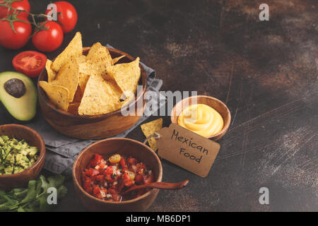 Mexikanisches Essen Konzept. Nachos - Mais, totopos Chips mit verschiedenen Saucen in mit Holz Schalen: Guacamole, Käse Sauce, Pico del Gallo Stockfoto