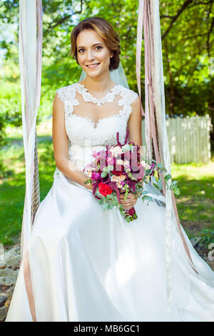 Gerne attraktive Frau Holding wedding bouquet und sitzen auf Schwingen am Sommergarten Stockfoto