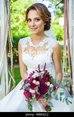 Gerne attraktive Frau Holding wedding bouquet und sitzen auf Schwingen am Sommergarten Stockfoto