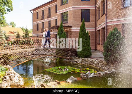 Hübscher Bräutigam und Braut gehen auf der Brücke in der Nähe von Brick House Stockfoto