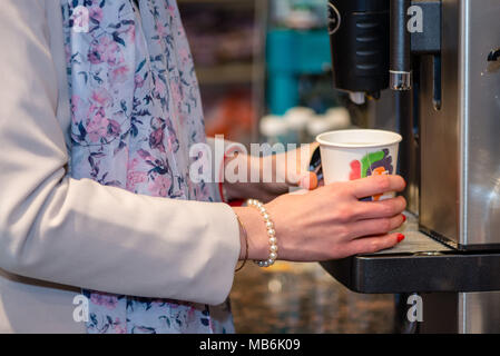 Close up Fotografie. Frauen Hände halten eine farbiges Papier Glas mit einem warmen Getränk. Stockfoto