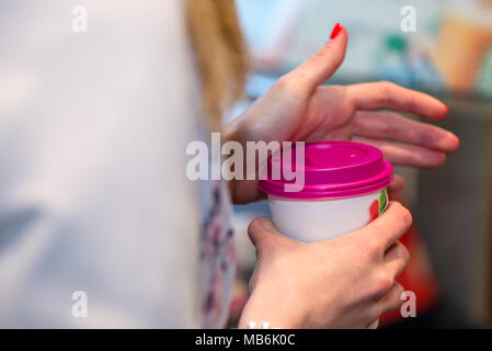 Close up Fotografie. Frauen Hände halten eine farbiges Papier Glas mit einem warmen Getränk. Stockfoto