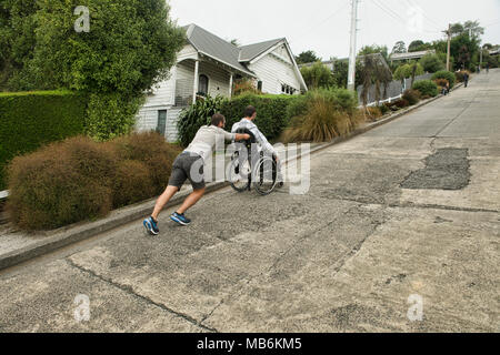 Freund seinen Kumpel Drücken in einem Rollstuhl bis Baldwin Street, der steilsten Strasse der Welt, Dunedin, Neuseeland Stockfoto