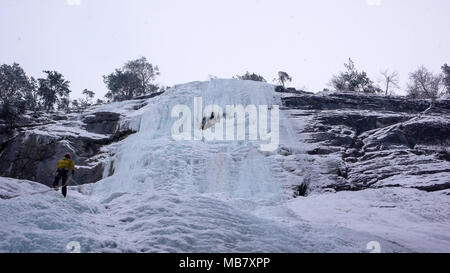 Männliche Bergführer Abseilen aus einem steilen gefrorenen Wasserfall nach einem ice Ausflug klettern Stockfoto