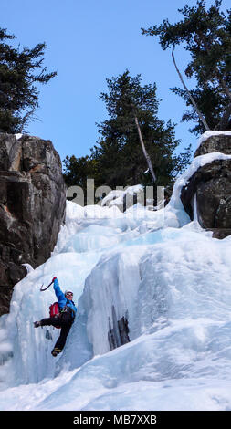 Männliche Eiskletterer in einer blauen Jacke auf einem wunderschönen gefrorenen Wasserfall Klettern in den Alpen, im tiefen Winter Stockfoto