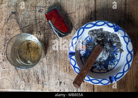 Ein Glas Whisky und eine Zigarre, ein Feuerzeug und ein Aschenbecher auf dem Tisch von oben genommen Stockfoto