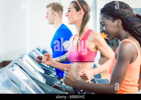 Seitliche Sicht auf eine glückliche Frau und ihr Training Gruppe am Laufband Stockfoto