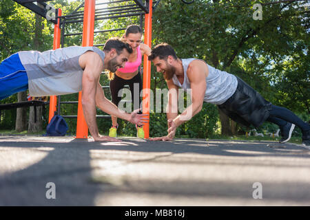 Zwei junge Männer klatschen Hände von ganzkörperstütz während Partner Training im Park Stockfoto