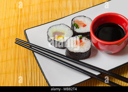 Drei sushi Rollen auf einer Platte mit einer Schüssel mit Sojasauce und Stäbchen Stockfoto