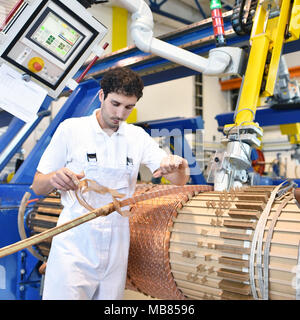 Junge Maschinenbau Arbeitnehmer eine Maschine bedienen für Wicklung Kupferdraht - Herstellung von Transformatoren in einer Fabrik Stockfoto