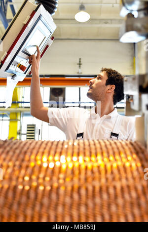 Junge Maschinenbau Arbeitnehmer eine Maschine bedienen für Wicklung Kupferdraht - Herstellung von Transformatoren in einer Fabrik Stockfoto