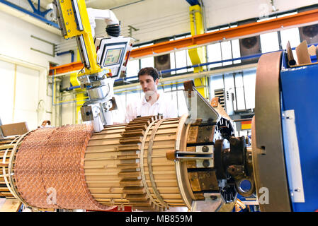 Junge Maschinenbau Arbeitnehmer eine Maschine bedienen für Wicklung Kupferdraht - Herstellung von Transformatoren in einer Fabrik Stockfoto